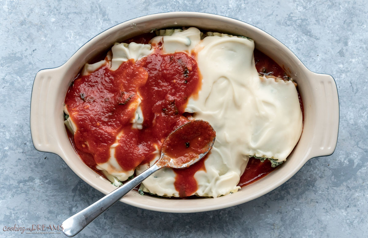 spoon spreading tomato sauce over the lasagna rollups