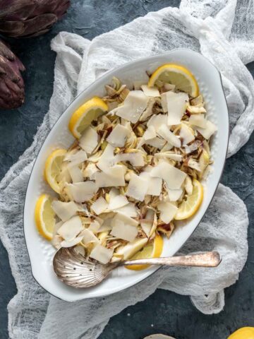 shaved artichoke salad with parmigiano arranged on an oval platter with lemon slices