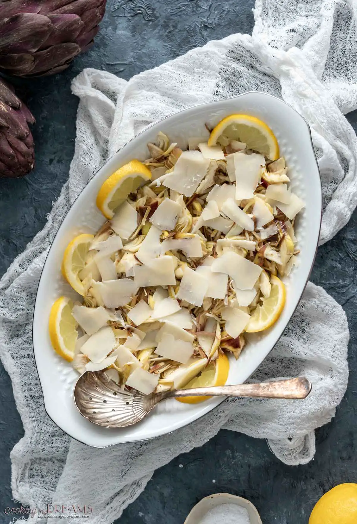shaved artichoke salad with parmigiano arranged on an oval platter with lemon slices
