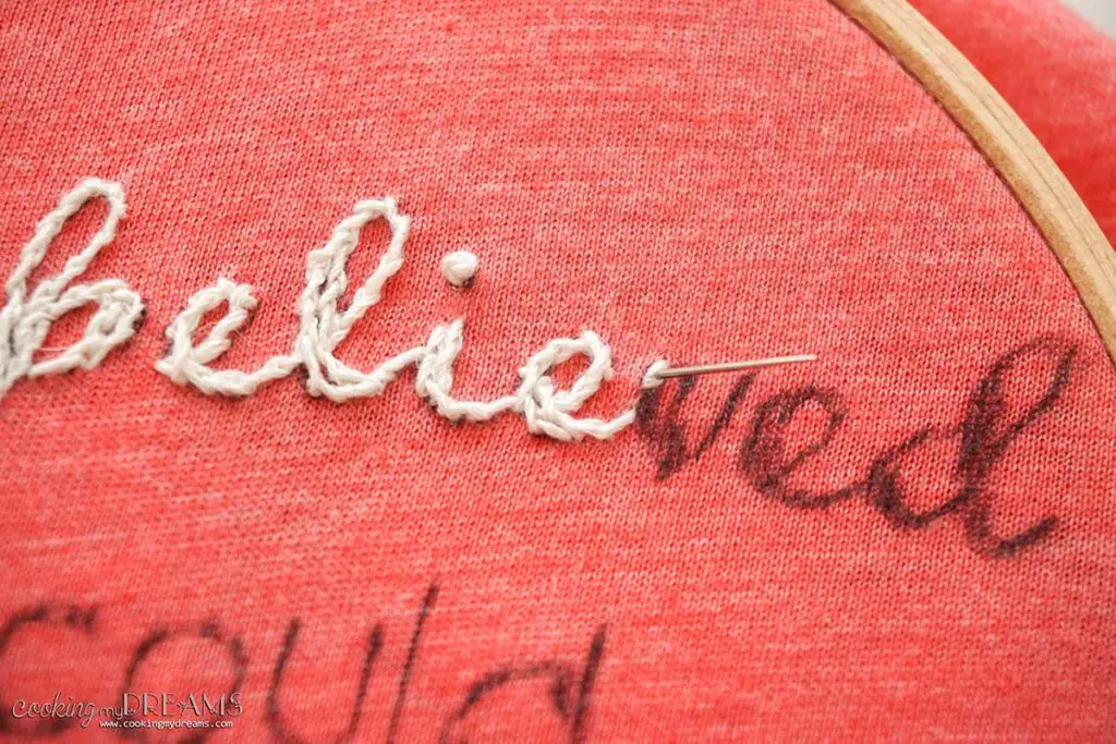 needle embroidering white text through a pink t-shirt