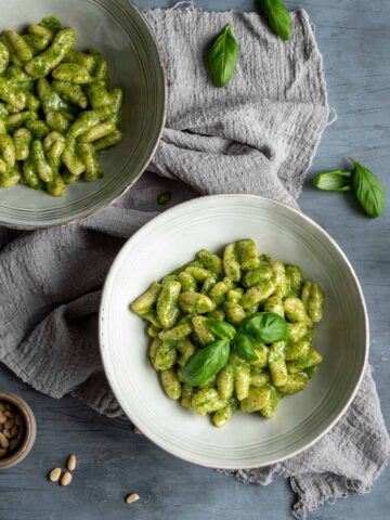 two bowls filled with creamy pesto gnocchi on a grey towel