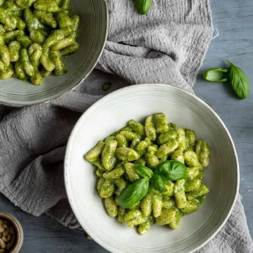 two bowls filled with creamy pesto gnocchi on a grey towel