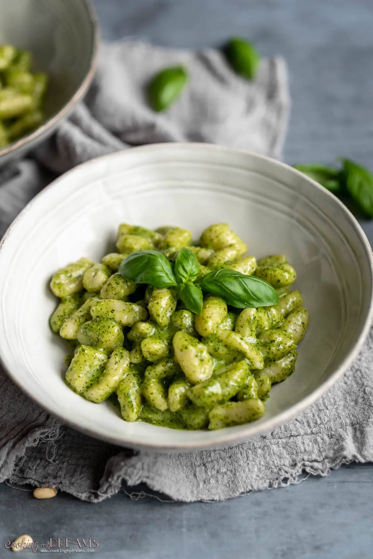 White bowl with creamy pesto gnocchi topped with fresh basil leaves