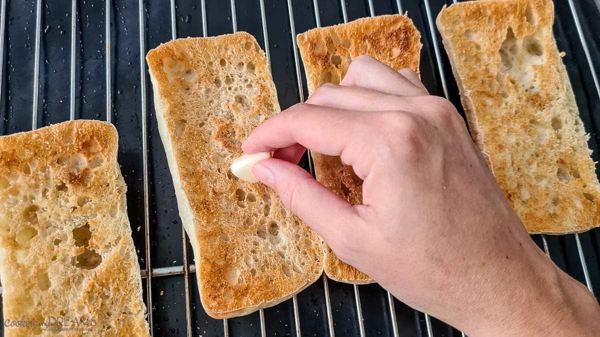 hand rubbing garlic on toasted bread slices