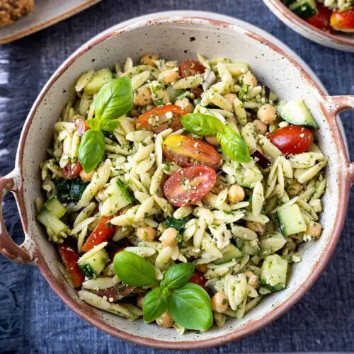 bowl of pasta salad with tomatoes and basil leaves on top