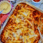 baked penne pasta with cheese, crushed pepper and other fixings on the side