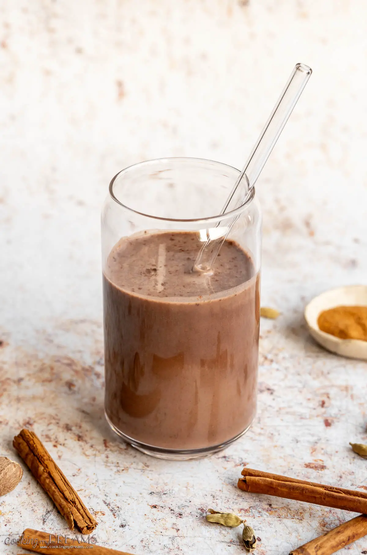 a glass of chocolate protein shake next to several spices
