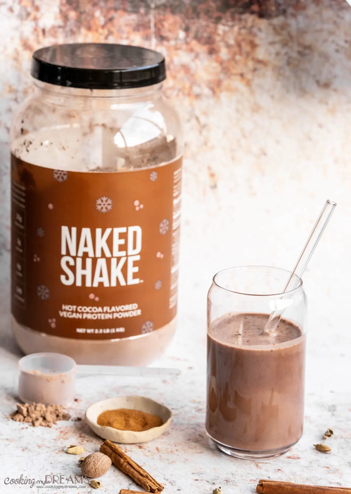 glass of chocolate protein shake next to protein powder tub