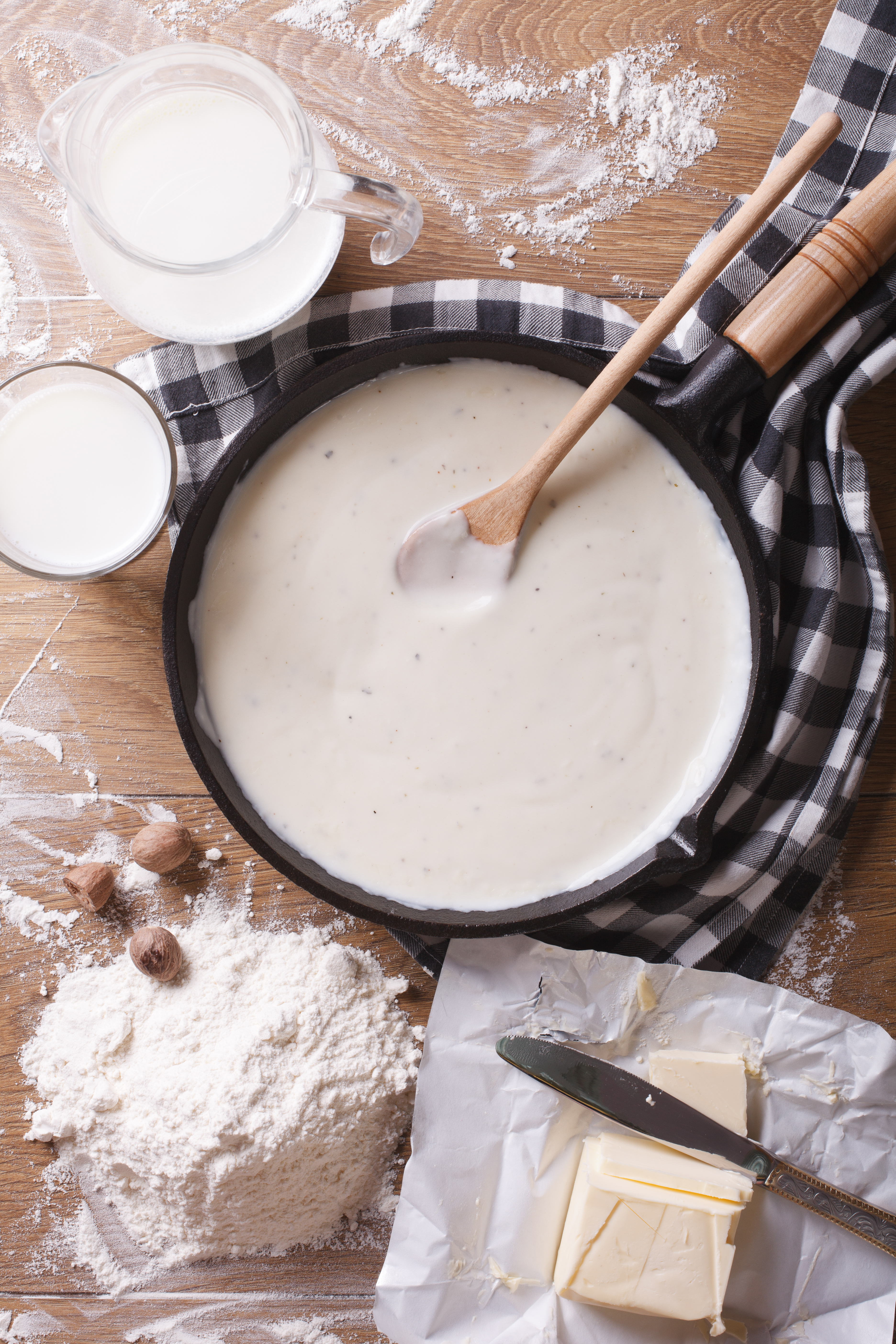 bechamel sauce in a pan with a wooden spoon next to the ingredients