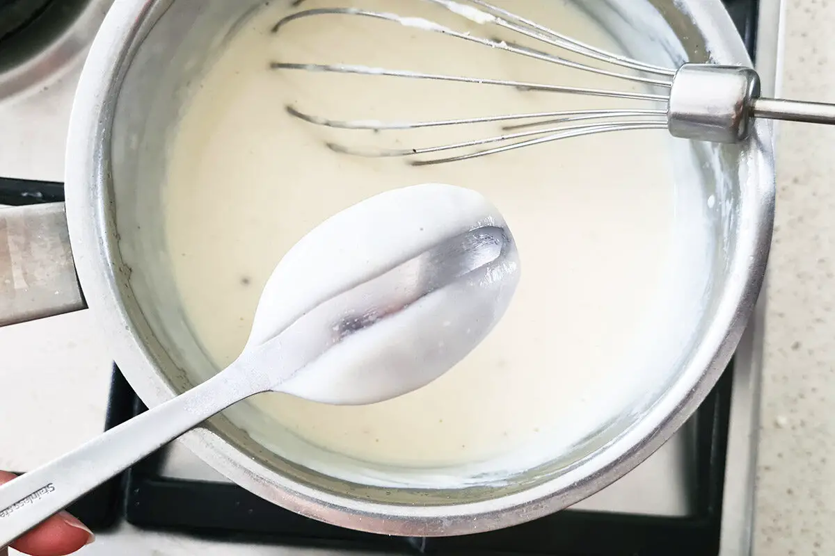 bechamel sauce in a pan with a whisk and a spoon