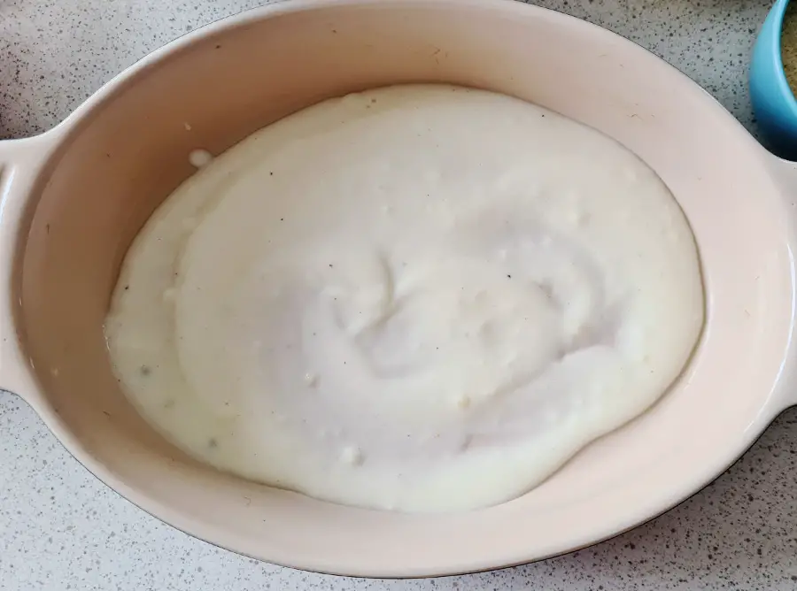 oval baking dish with a layer of bechamel sauce
