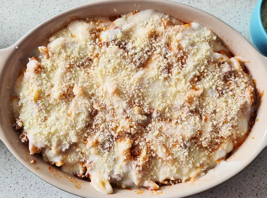 grated parmigiano cheese layered on top pf pasta in a casserole