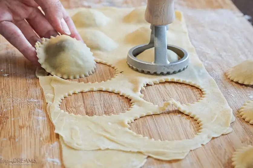 hand holding a raw ravioli on a wooden board