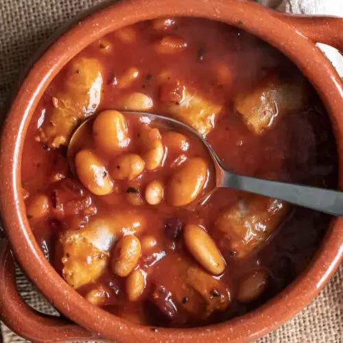 spoon in a terracotta bowl with sausage and beans stew