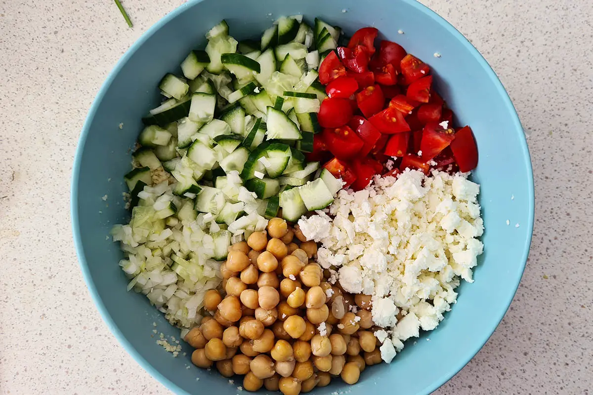 large bowl of couscous topped with cucumbers, tomatoes, feta, chickpeas and onion