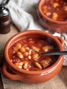 tuscan beans and sausage stew in a terracotta bowl with a spoon