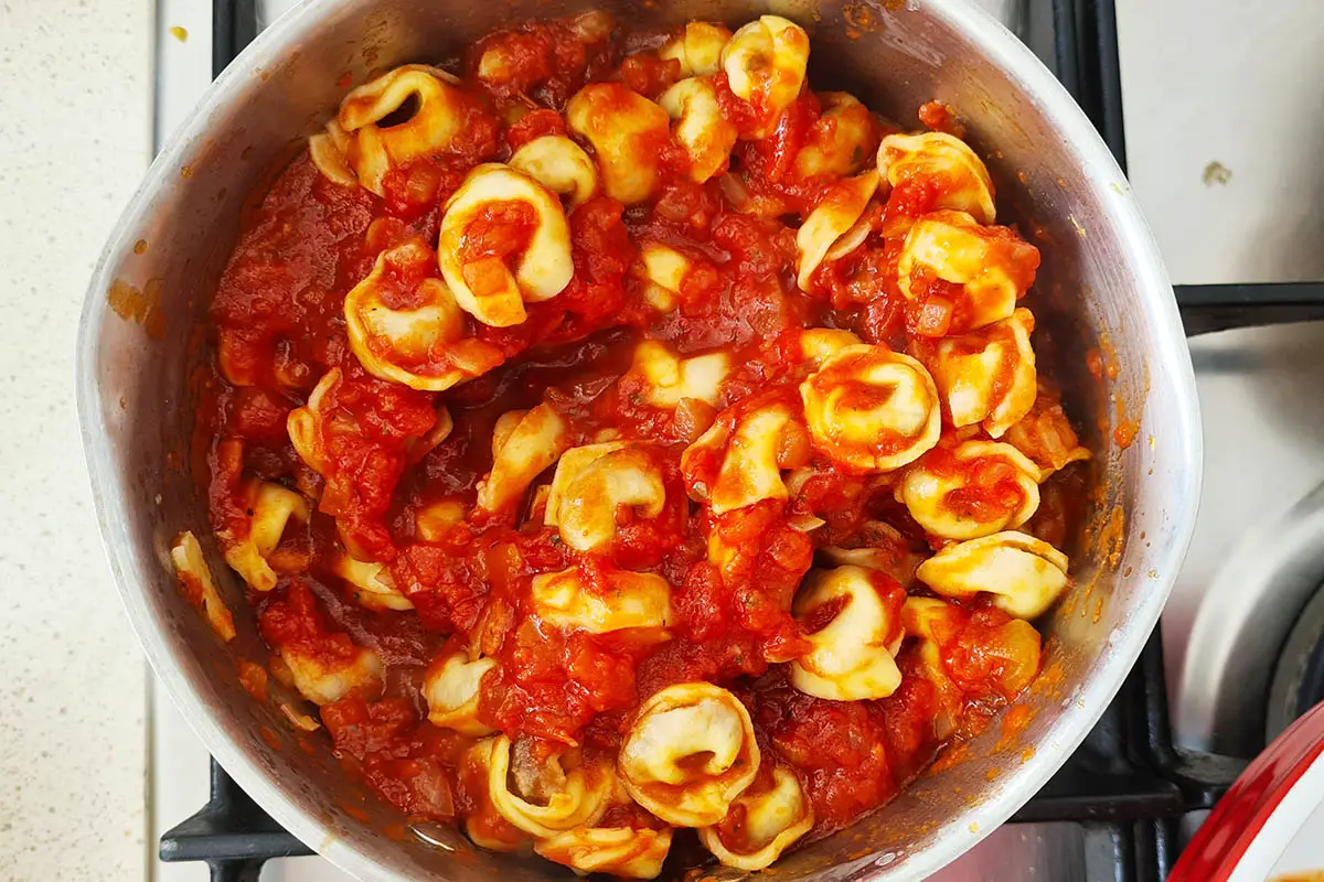 tortellini being mixed with tomato sauce in a pan