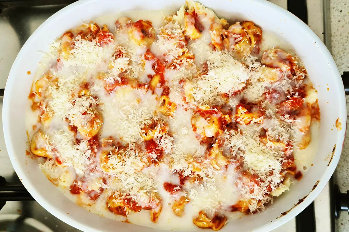 tortellini with tomato sauce, white sauce and grated parmesan in a baking dish