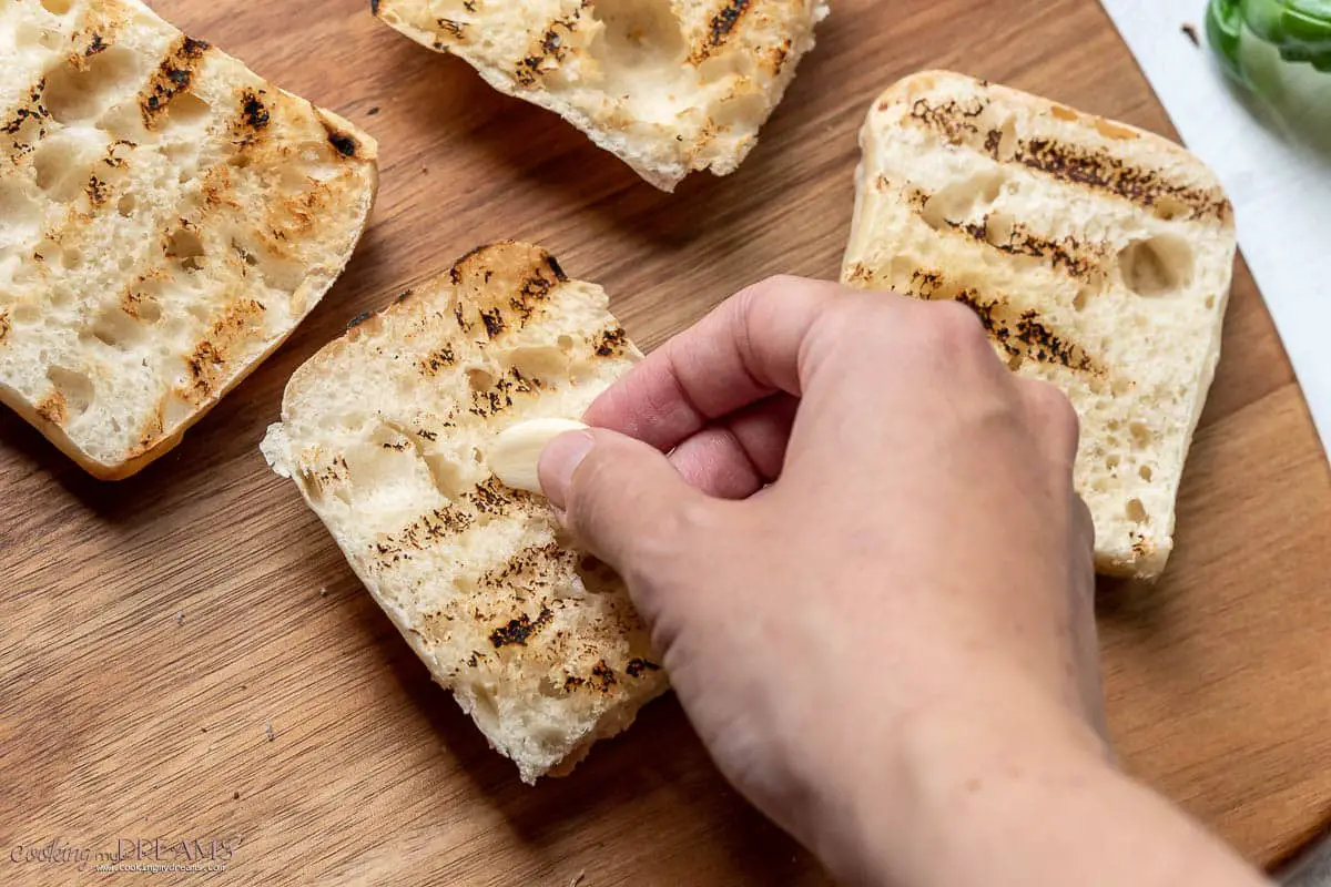 hand rubbing garlic on toasted bread slices.