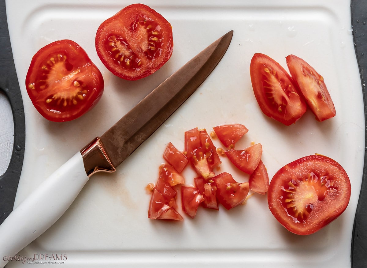 tomatoes being chopped on a cutting boeard with a knife