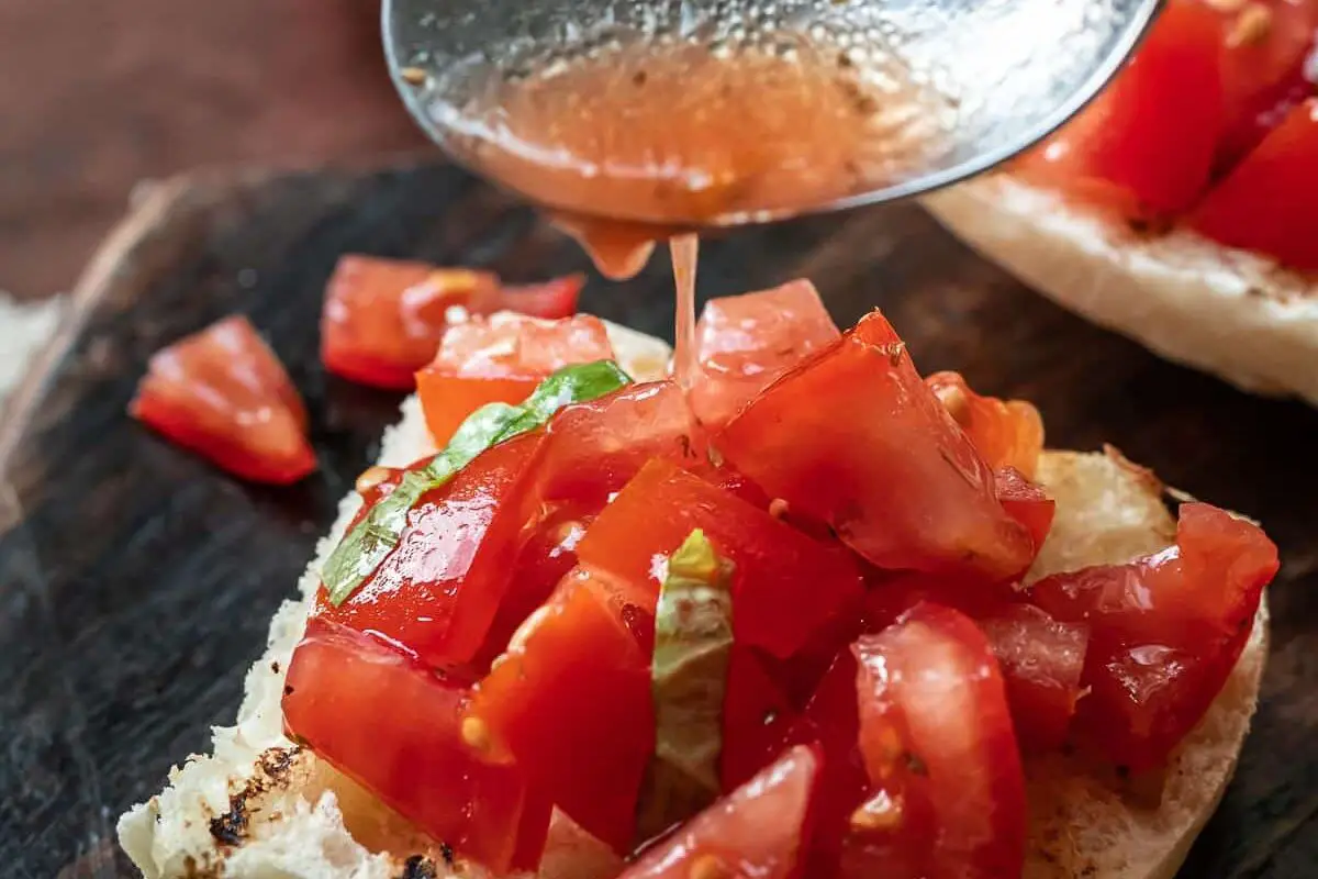 spoon drizzling olive oil over a tomato bruschetta.