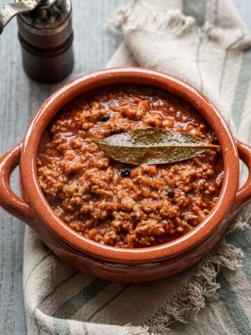 tuscan ragù sauce in a terracotta pot with a bay leaf on top.