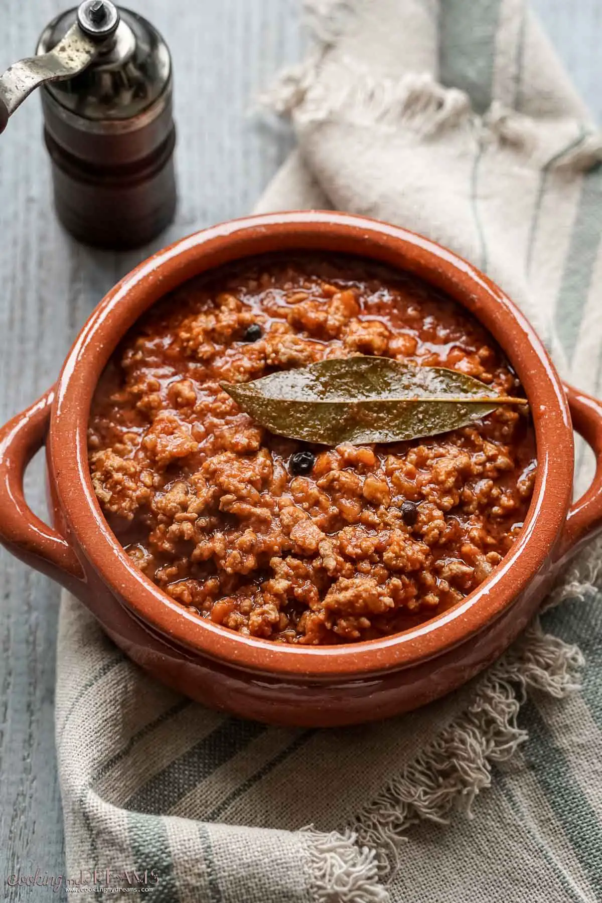 tuscan ragù sauce in a terracotta pot with a bay leaf on top.