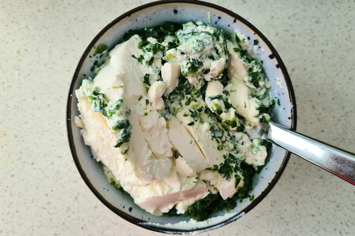 spoon mixing spinach and ricotta in a bowl.