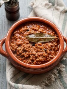 tuscan ragù sauce in a terracotta pot with a bay leaf on top.