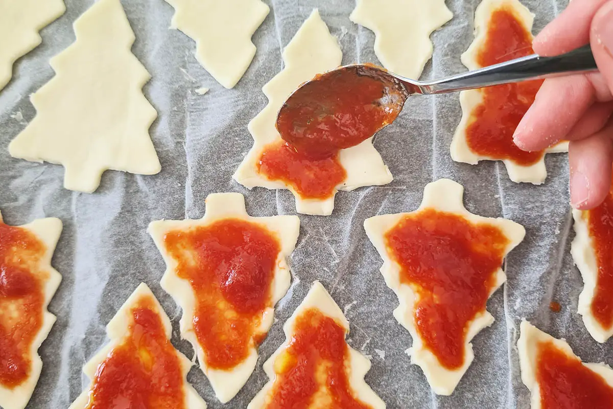 spoon pouring pizza sauce on the puff pastry trees,