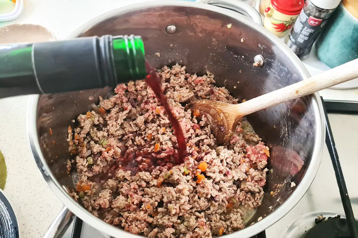 red wine is added to the pot with the ground meat.