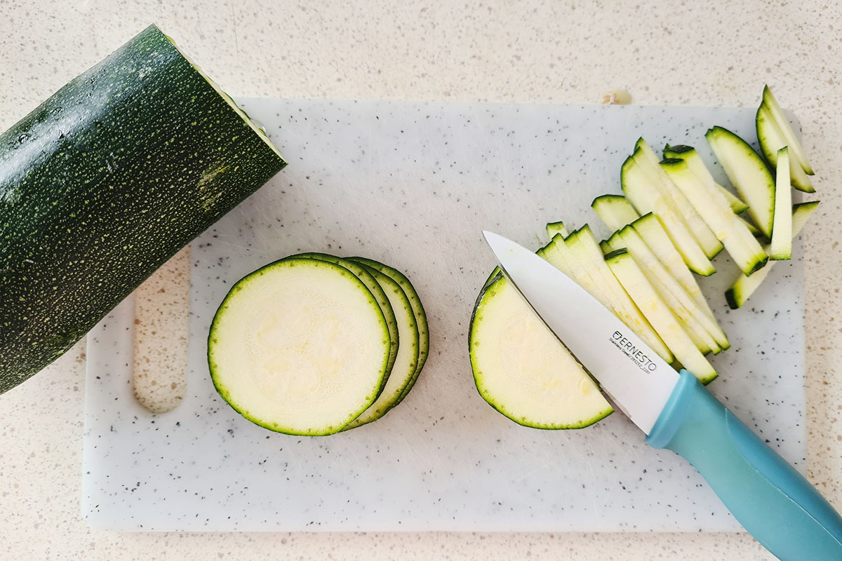 zucchini being cut into matchsticks on a cutting board