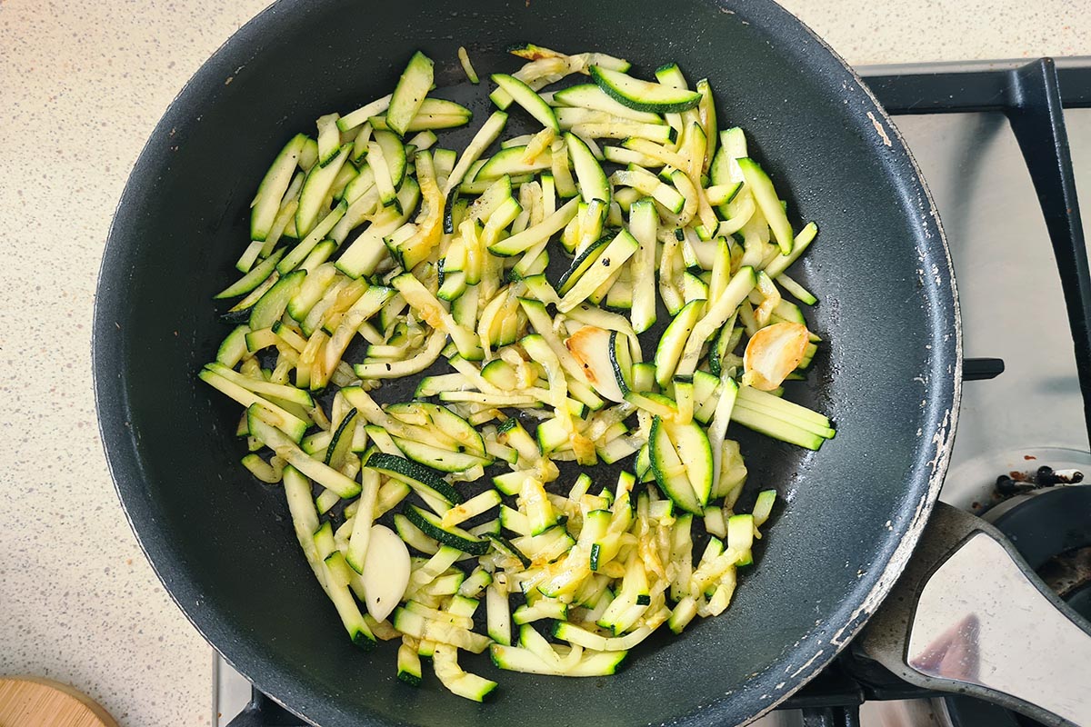 zucchini cooking in a pan with oil and garlic.