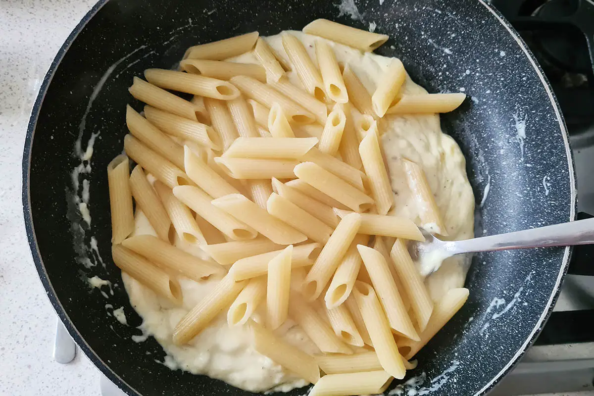 pasta is tossed in the pan with the cheese sauce.