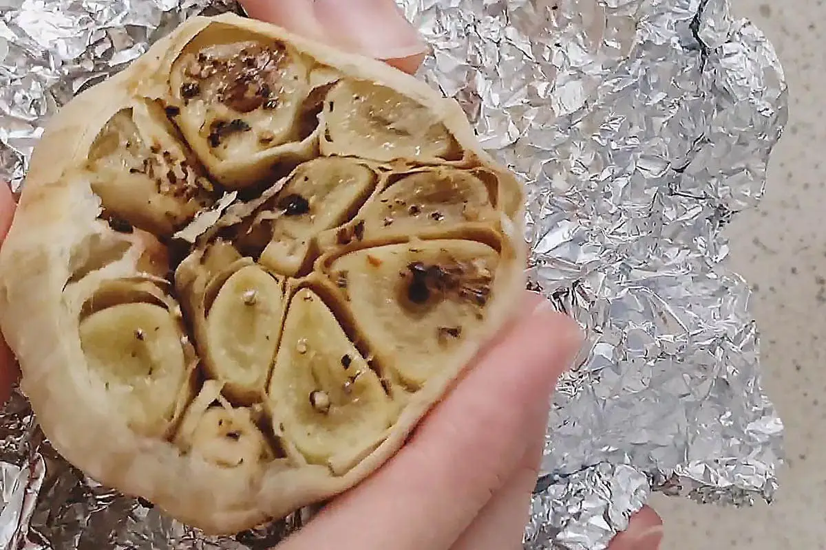 hand holding roasted garlic in foil.