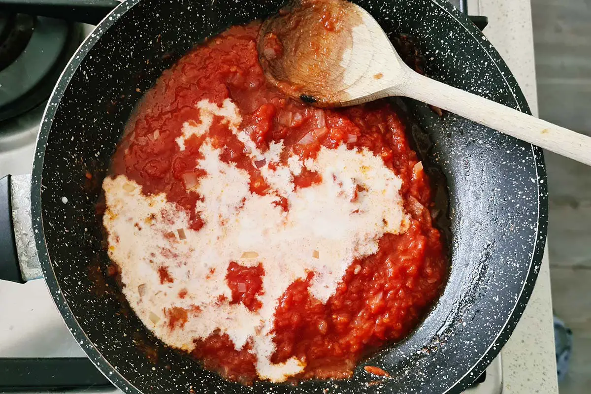 spoon in the pan with tomato sauce and cream.