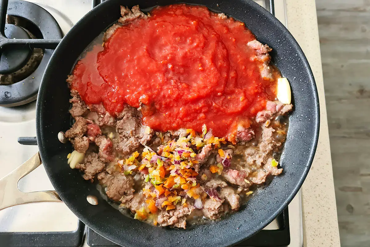 tomato sauce and seasonings are added to the pan with the sausage.