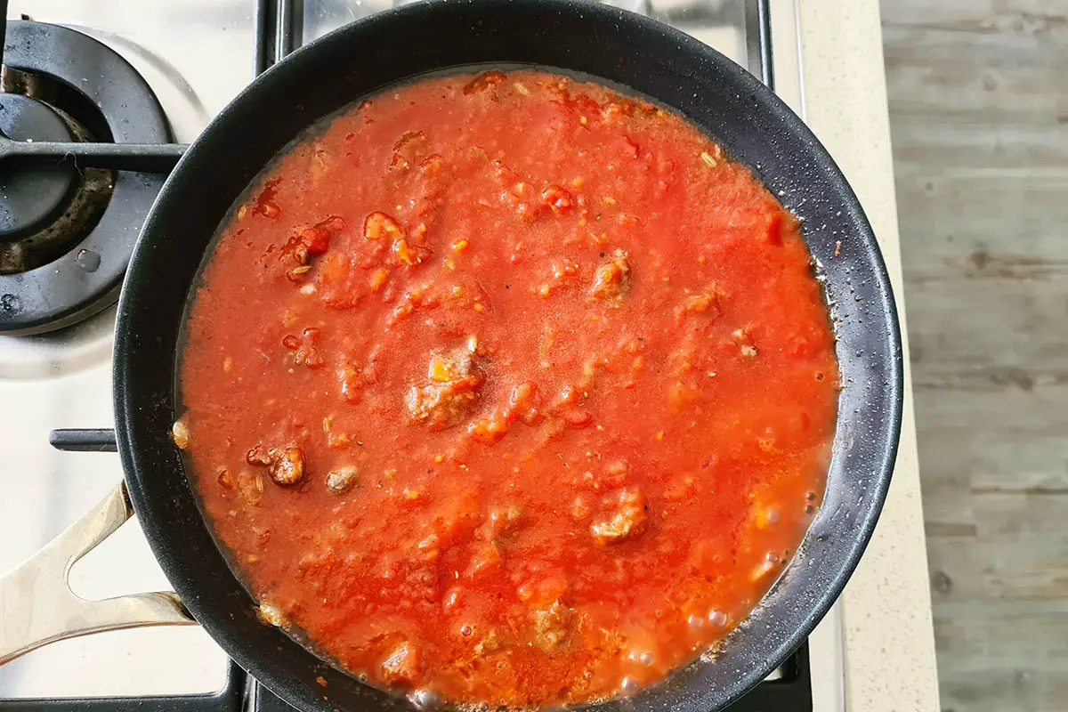 the sausage pasta sauce is simmering in the pan.