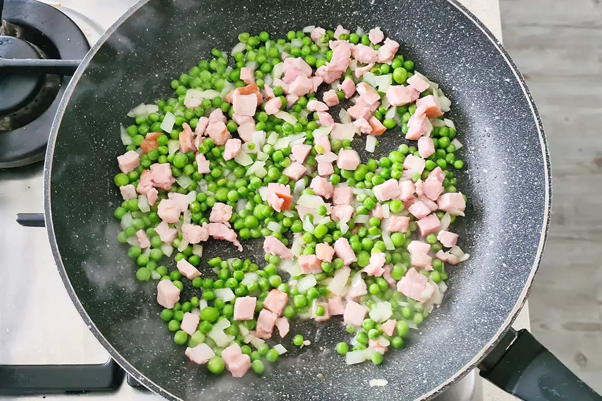 peas, onions, and ham are cooking in a pan.