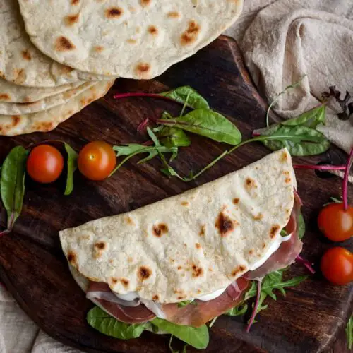 A folded piadina filled with prosciutto and salad, on a wooden board.