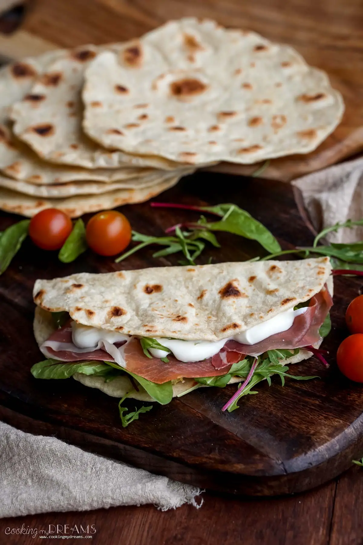 A folded piadina filled with prosciutto and salad, on a wooden board.