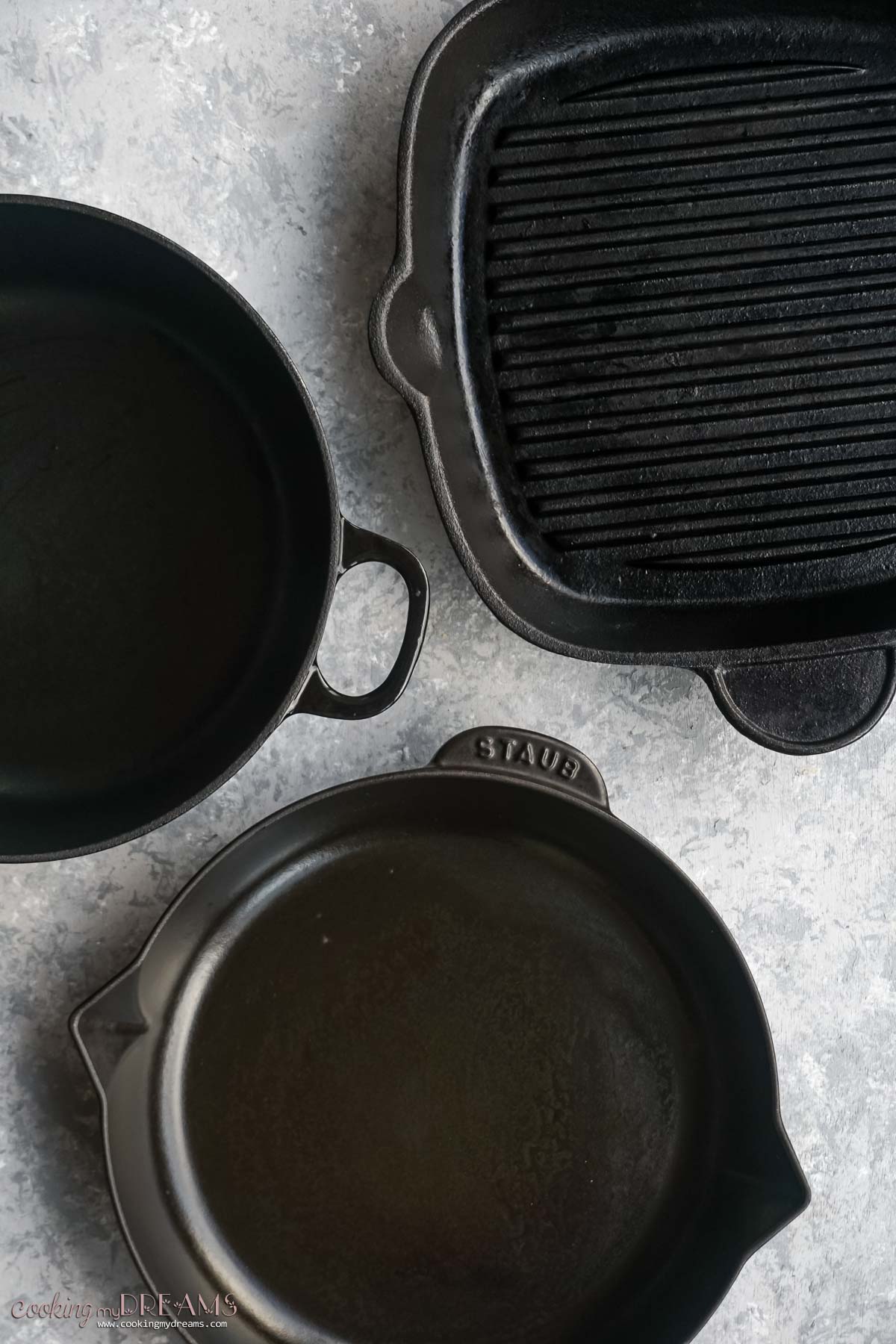 a cast iron skillet next to a cast iron dutch oven and cast iron grill pan.