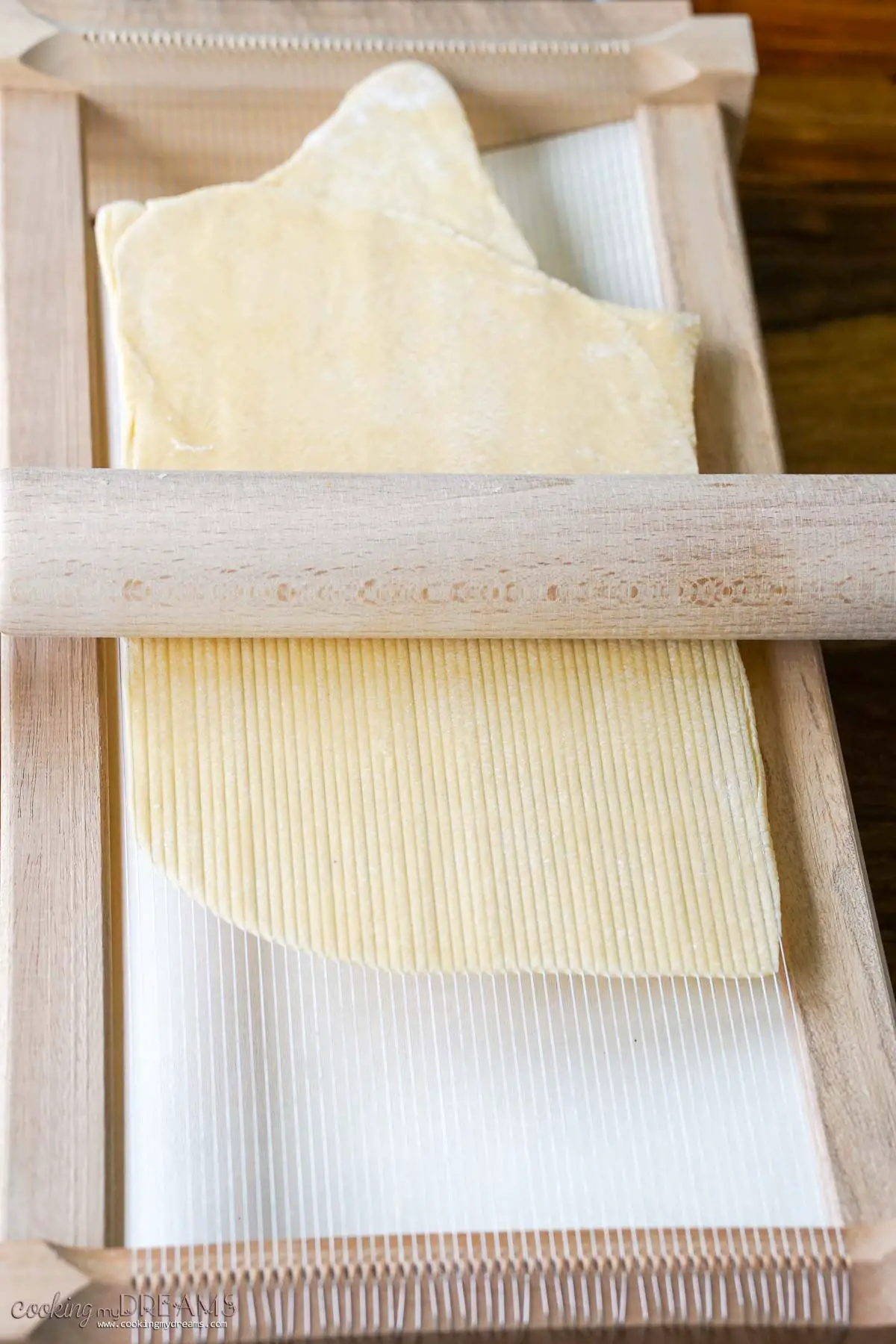 rolling pin stretching pasta dough over a chitarra tool