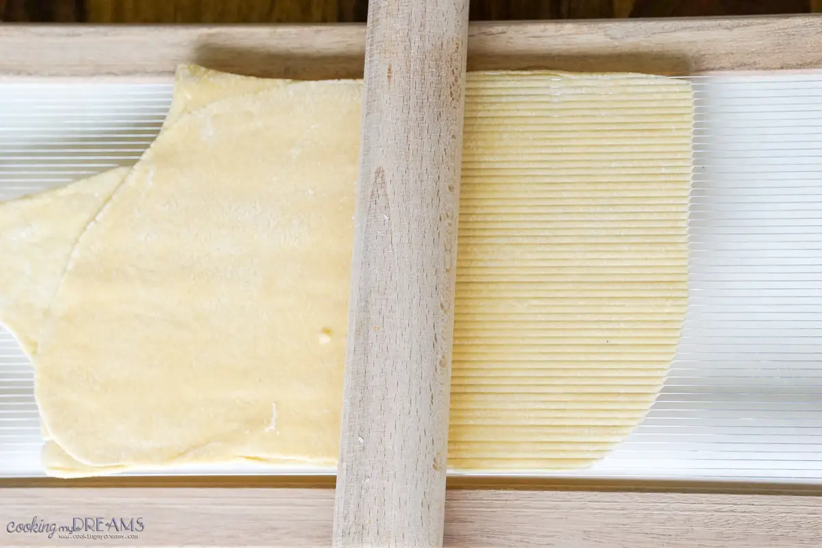 rolling pin stretching pasta dough over a chitarra pasta tool