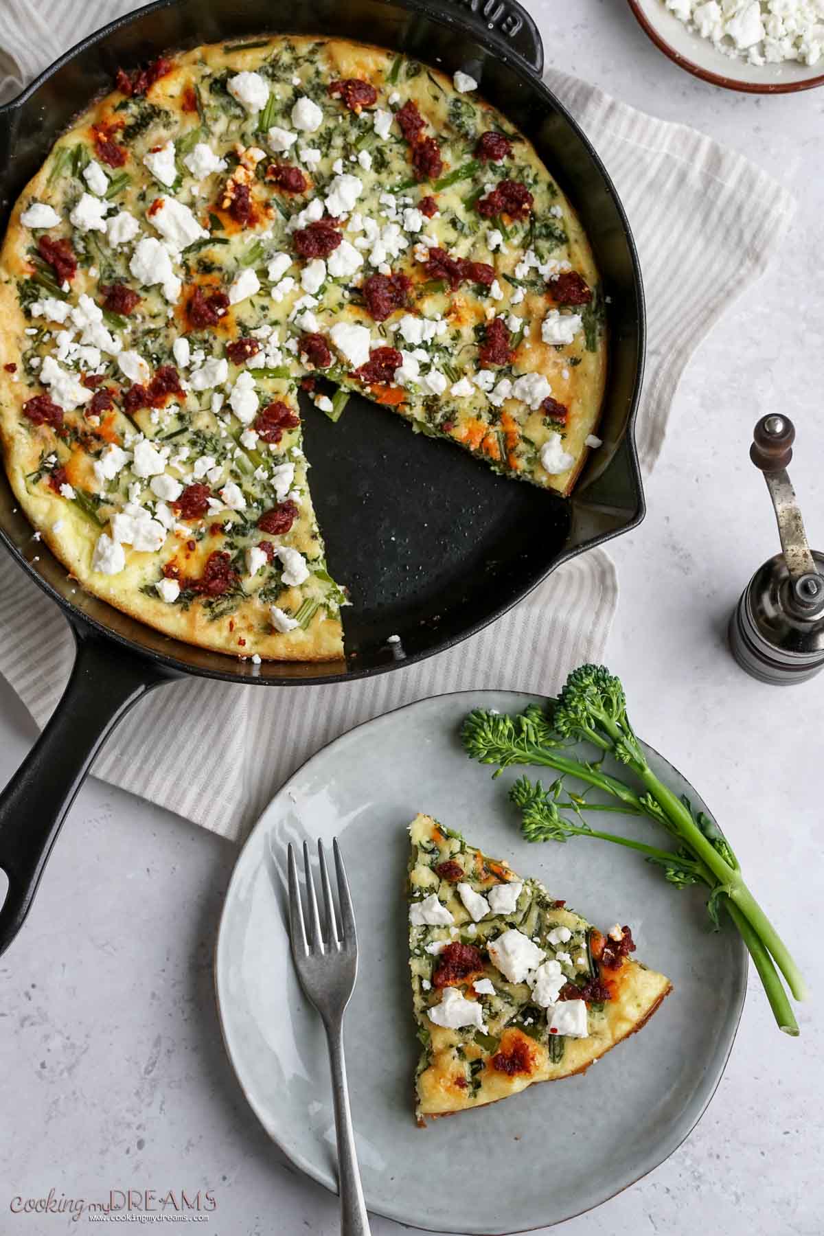 a slice of broccolini frittata on a plate, next to a skillet.