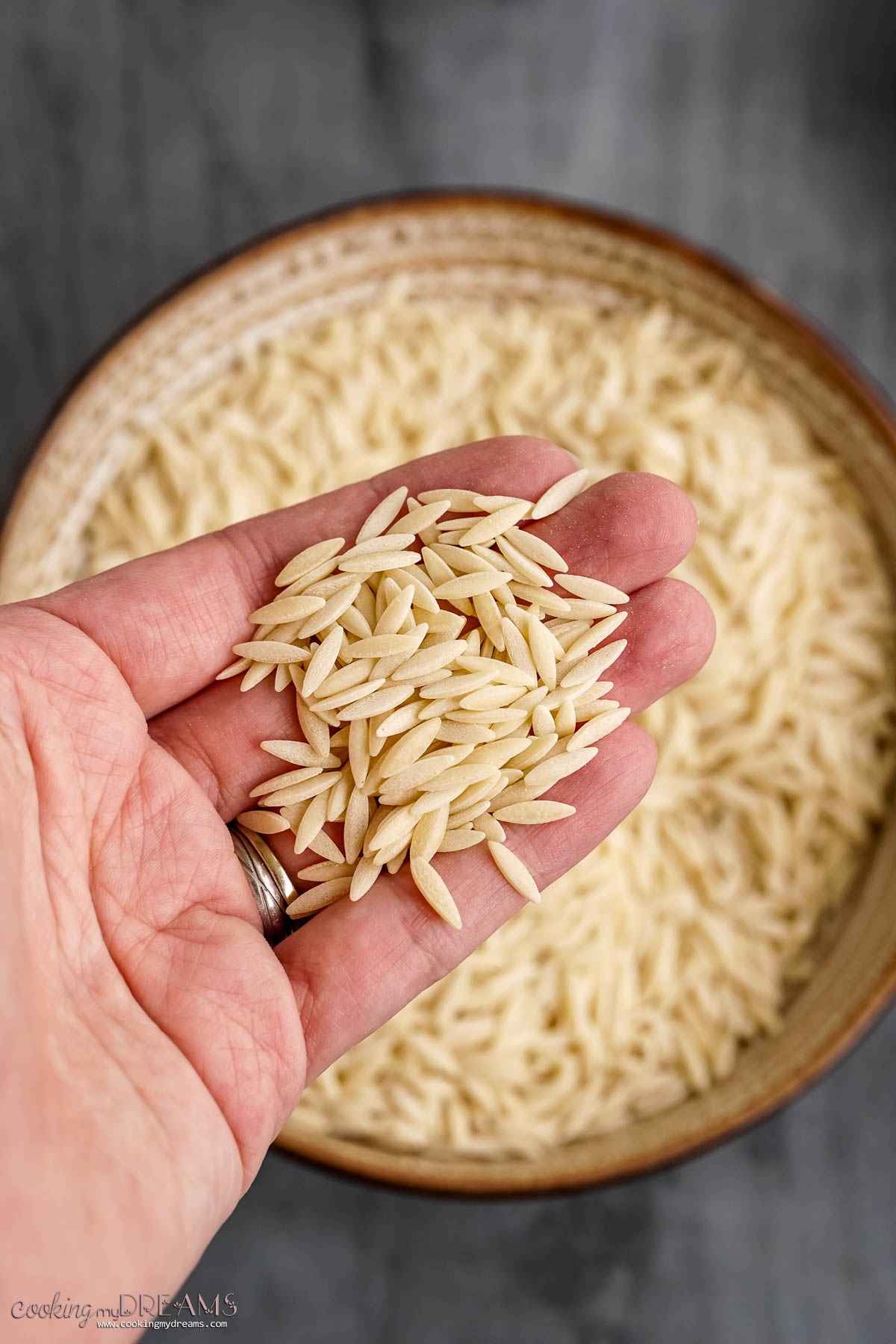 hand holding some dried orzo pasta over a full bowl.