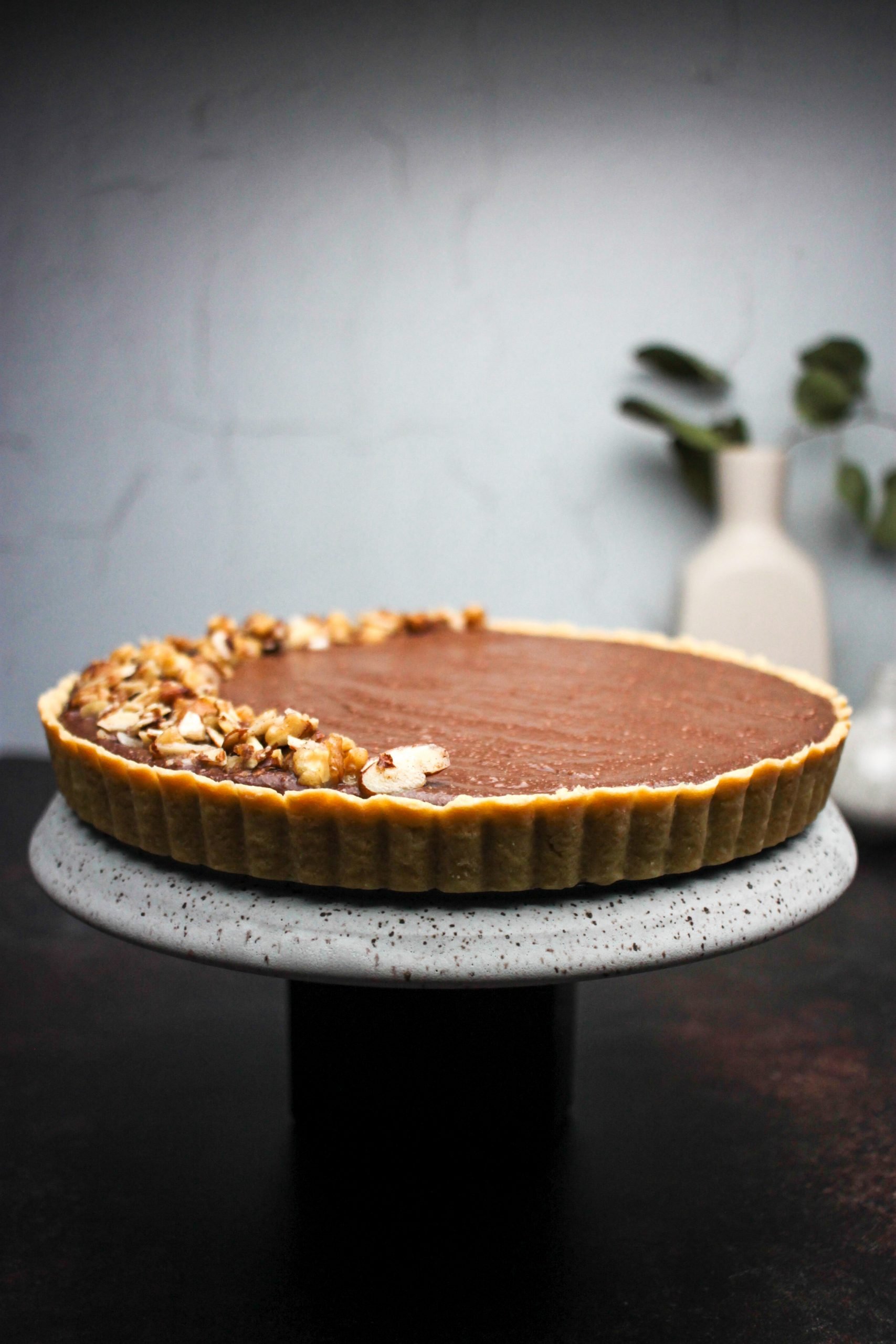 nutella ricotta tart topped with nuts, on a marble stand.