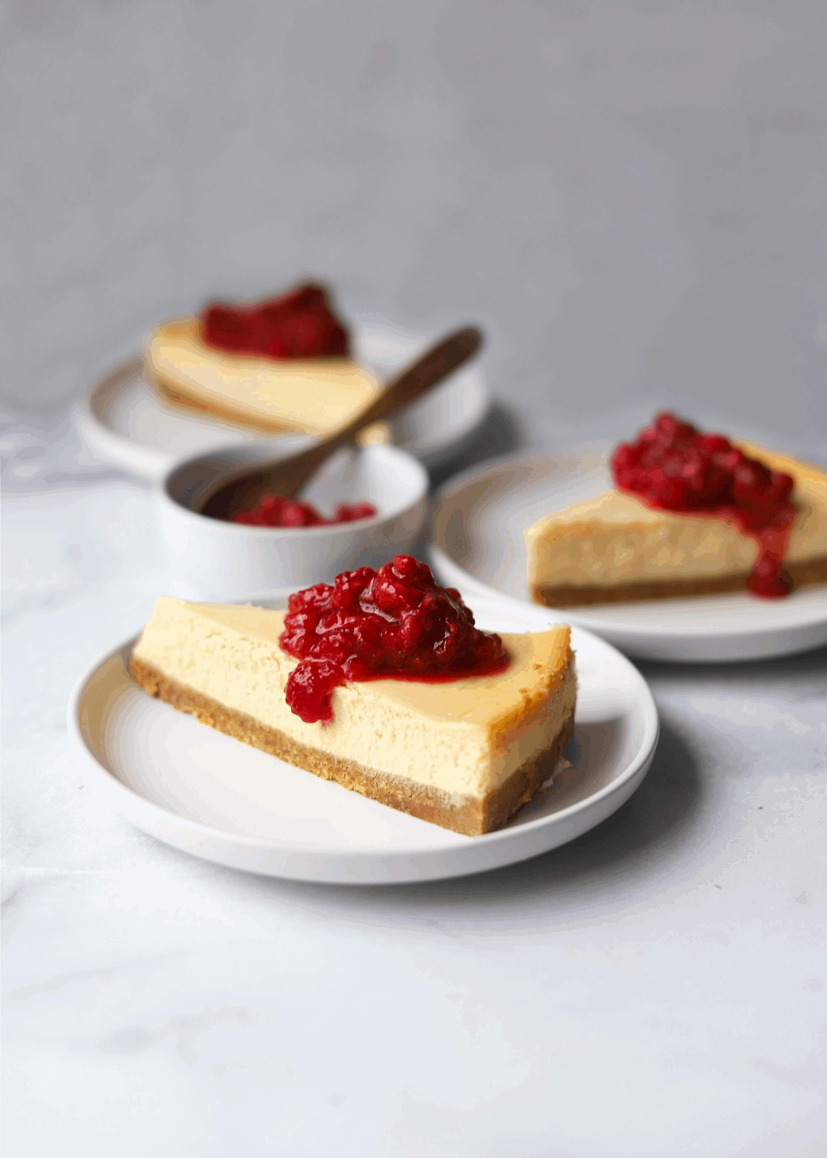 three plates with ricotta cheesecake topped with raspberries.