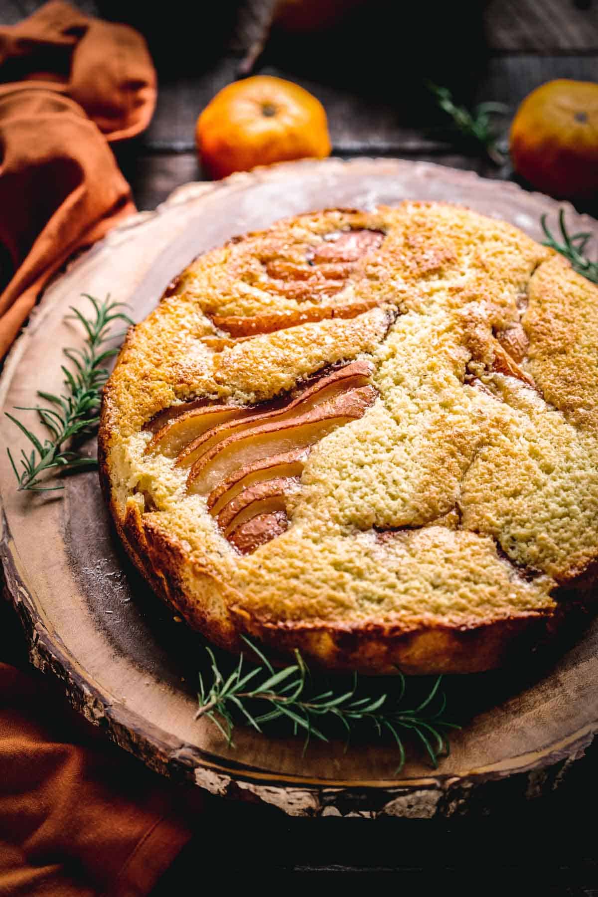 ricotta pear cake on a wooden stand surrounded by rosemary.