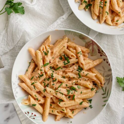 two dishes of penne al salmone topped with parsley.